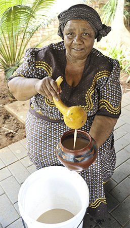 Xhosa woman brewing and serving umqombothi beer